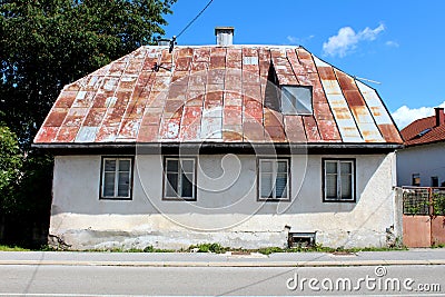 Front view of abandoned small urban family house on cracked stone and concrete foundation with rusted metal roof tiles Stock Photo
