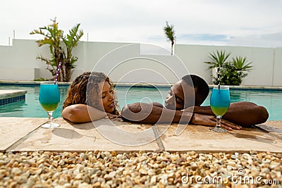 Couple with cocktail glasses leaning on the edge of a swimming pool Stock Photo