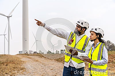 Front view of african american man and woman engineers in uniform discuss and use tablet working stand near wind turbines Stock Photo