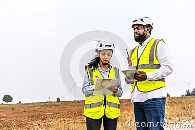 Front view of african american man and woman engineers in uniform discuss and use tablet working stand near wind turbines Stock Photo