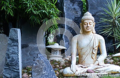 Front view of a Buddha statue with blue grey rocks in the background and bamboo trees. Enlightment concept Stock Photo