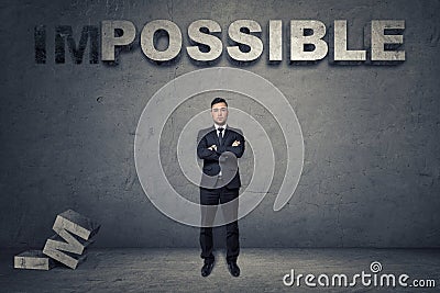 Front view of a buisnessman standing with folded arms under big 3d concrete word 'possible' Stock Photo