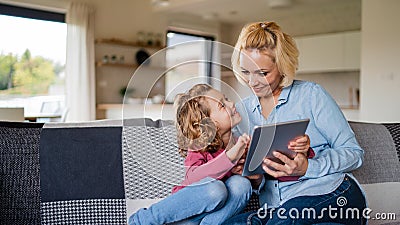 A cute small girl with mother on sofa indoors at home, using tablet. Stock Photo