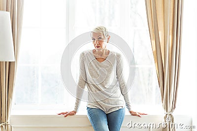 Cheerless senior female sitting on the sill Stock Photo