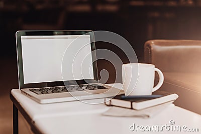 Front view. Empty workplace. On white coffee table is laptop with blank screen, cup of coffee, notebook, pen, newspaper. Stock Photo