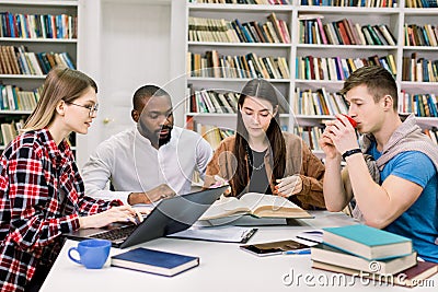 Front view of four good-looking modern smart mixed race students which are sitting in the reading room of library and Stock Photo