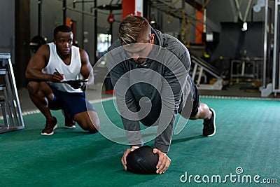 Male trainer writing on clipboard while male athletic exercising with exercise ball Stock Photo