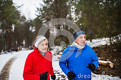 A front view of senior couple jogging in snowy winter nature. Stock Photo