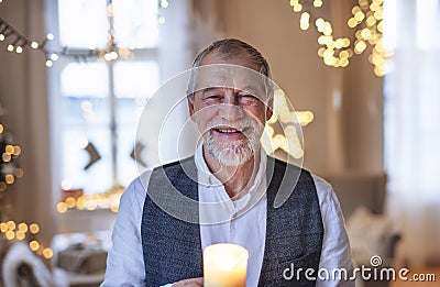 Front view of happy senior man indoors holding candle at Christmas. Stock Photo