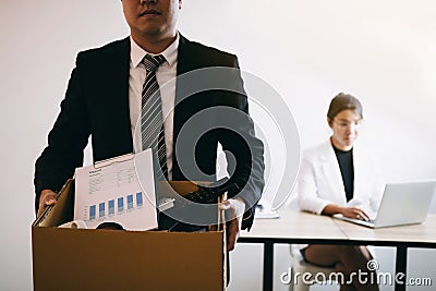 Front view with the male employee standing holding office supplies in the paper box going to submit a resignation letter while a Stock Photo