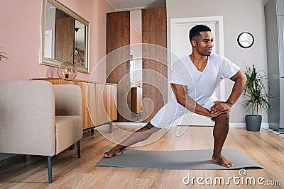 Front view of smiling strong African-American man doing side lunge exercise at home Stock Photo