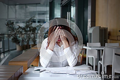 Front view of stressed frustrated young Asian business woman covering face with hands on the desk in office Stock Photo