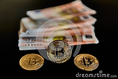 Front view of three Bitcoin coins, next to a group of Euro banknotes, on a black background. Concept of money, power, economics, Stock Photo