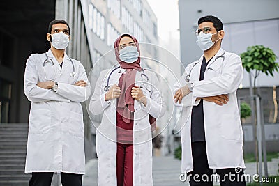 three multiethnic healthcare workers wearing face masks, posing with arms crossed outdoors Stock Photo