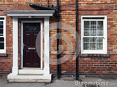 front view of a typical old small english terraced brick house with black painted door and white portico and windows Stock Photo