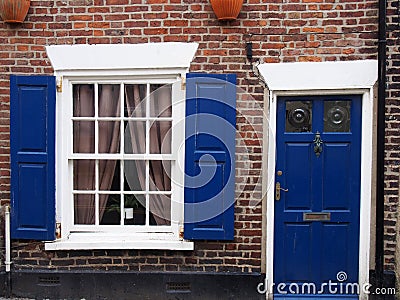 front view of a typical old small english terraced brick house with blue painted door and shutters Stock Photo