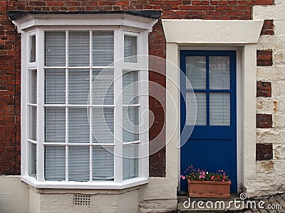 front view of a typical old small english terraced brick house with blue painted door white bay windows Stock Photo