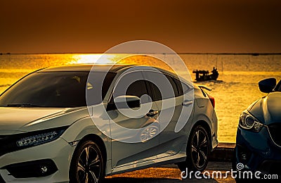 Front view of white and blue compact car parked on concrete road by sea beach at sunset sky. Electric and hybrid car technology. Stock Photo
