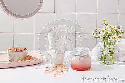 Front view of a white tube and jar without label arranged with a bowl of pink himalayan salt and flower pot Stock Photo
