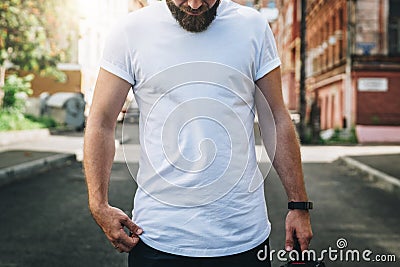 Front view. Young bearded millennial man dressed in white t-shirt is stands on city street. Mock up. Stock Photo