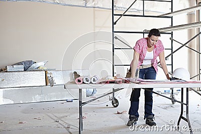 Front view of young female contractor looking at building plans at table Stock Photo