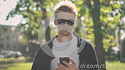 Front view of young man in sunglasses taking smartphone from his pocket stock video Front view of young man in sunglasses taking smartphone from his pocket stock video