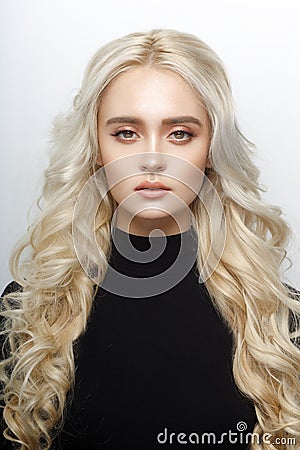 Frontal portrait of a cute blonde girl, with delicate make up, curly shiny long hair, isolated of a white background. Stock Photo