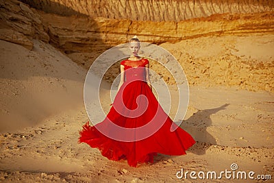 Beauty portrait of a sensual young blonde woman, wear in red long flying dress, posing in a sand desert. Stock Photo