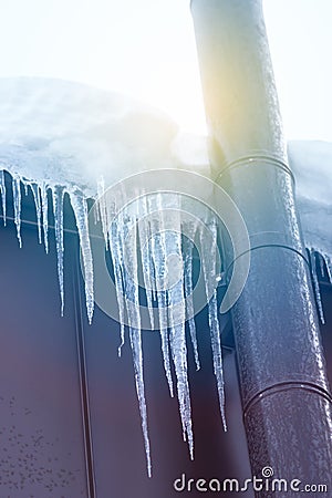 Frosted chimney pipe and icicles hanging from eaves of roof on cold day in snow and sky background Stock Photo