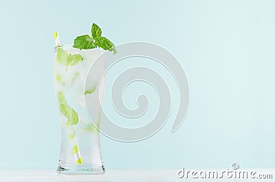 Frosty mint lemonade with green leaf, ice cubes, striped straw, mineral water in elegant glass on white wood table, mint color. Stock Photo