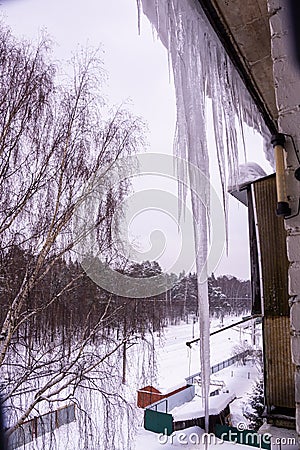 On a frosty winter day, large beautiful icicles hang from the snow-covered roof of the house. Snow on the roof. Stock Photo