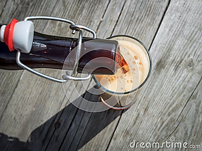Frothy dark beer pouring into tall glasses from a brown glass bottle in summer garden on rustic wooden table Stock Photo