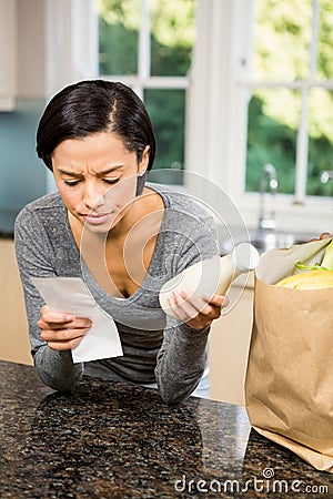 Frowning brunette holding receipt and milk Stock Photo