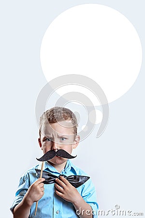 Frowning serious boy in a light shirt put a mustache on a stick and a bow tie on his face to make him look older Stock Photo