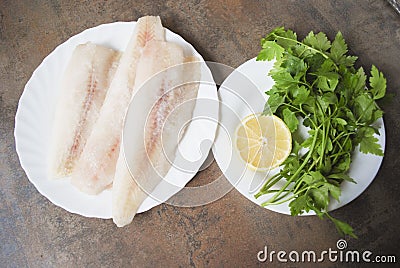 Frozen Alaska Pollock fillet with lemon and parsley on white plate. Stock Photo