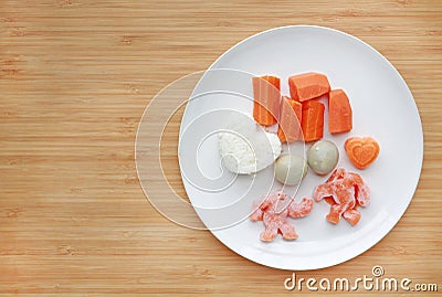 Frozen baby food homemade and raw food in white plate, Sliced carrot egg and rice for mashed on wooden board Stock Photo