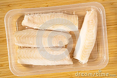 Frozen cod fish loins in vacuum package on the cutting board. Top view Stock Photo