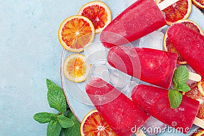 Frozen fruit juice. Homemade citrus ice cream or popsicles decorated mint leaves and orange slices on blue table top view. Stock Photo