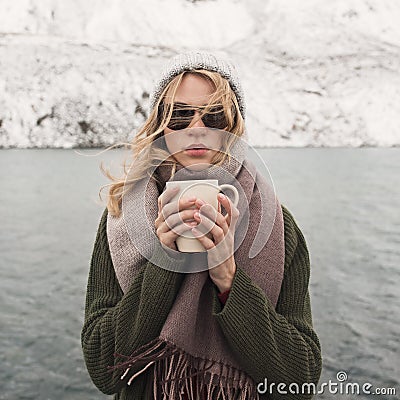 Frozen girl holds a cup of hot coffee. Mountain lake Stock Photo