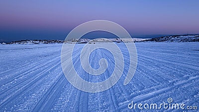 Frozen Lake Covered with Snow on a Winter Evening, with Snowmobile Tracks Stock Photo