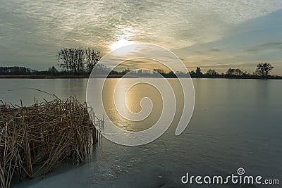 Frozen lake with dry reeds, sunset and clouds on the sky Stock Photo