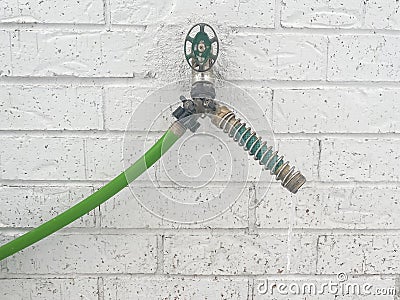 Frozen outdoor water spigot on white brick wall background with long ice dripping from garden hose protector coil spring Stock Photo