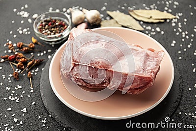 Frozen piece of raw meat on plate on black table. Rime on product, thawing Stock Photo
