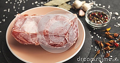 Frozen piece of raw meat on plate on black table. Rime on product, thawing Stock Photo