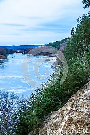 Frozen river covered with snow and ice, top view. Sandy hill with pine trees. Stock Photo