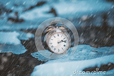 Frozen time. A clock on an ice next to the water. Extreme weather situation. Snow falling on a clock in a nature. Stock Photo