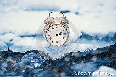 Frozen time. A clock on an ice next to the water. Extreme weather situation. Snow falling on a clock in a nature. Stock Photo