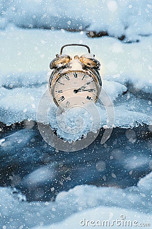 Frozen time. A clock on an ice next to the water. Extreme weather situation. Snow falling on a clock in a nature. Stock Photo