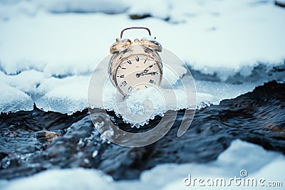 Frozen time. A clock on an ice next to the water. Extreme weather situation. Snow falling on a clock in a nature. Stock Photo