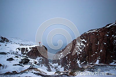 Frozen waterfall on the background of hills on the Kola Peninsula and a man standing on the edge of the cliff and looking into the Stock Photo